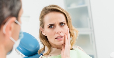 Woman in dental chair holding her cheek in pain